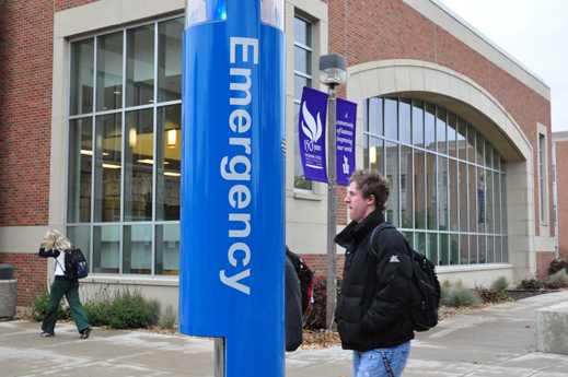 Student walking in front of a blue emergency phone on campus